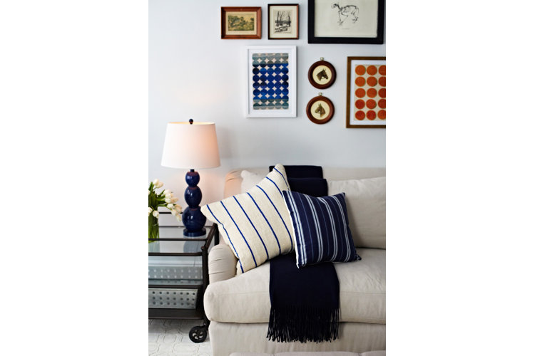 A beige linen sofa with a gallery wall above, black draped blanket, and blue and white striped pillows.