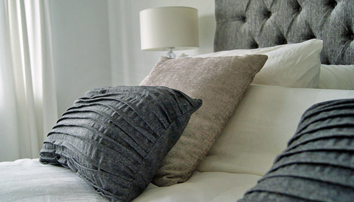 A bed decorated with accent pillows and bed linens in grey