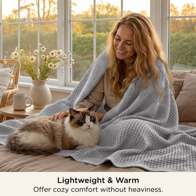 Gray waffle-weave cotton throw blanket draped over a woman sitting on a bed.