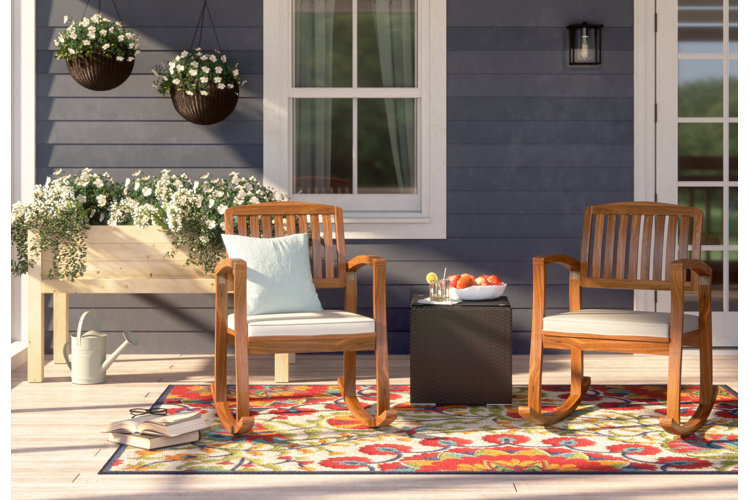 back porch with two teak rocking chairs, floral outdoor rug, and hanging basket planters