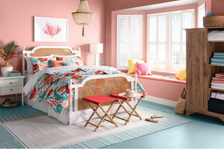 Bright coastal bedroom with a wicker bed, orange and teal floral bedding, pink walls, and a teal floor.