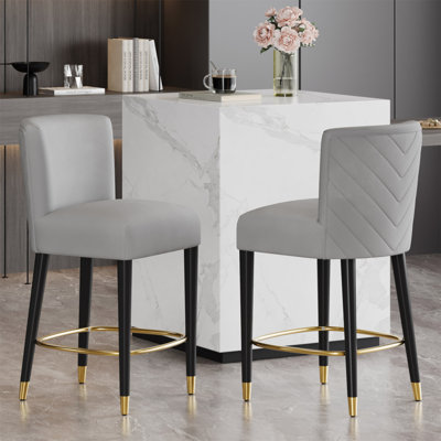 Le tabouret de 27 pouces au design moderne avec un tissu lisse et léger et un repose-pieds circulaire avec une finition dorée crée un look sophistiqué et luxueux