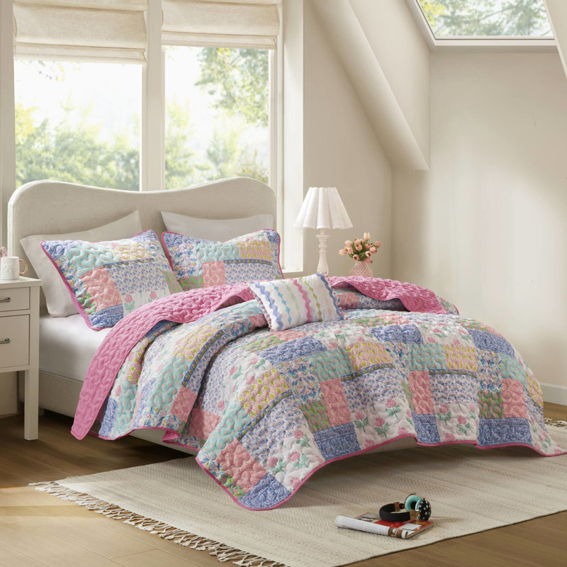 Couette rose à motifs floraux et à rayures audacieux, réversible pour une décoration polyvalente, en microfibre douce. Face avant patchwork ludique, revers uni apaisant. Confortable et facile à superposer.