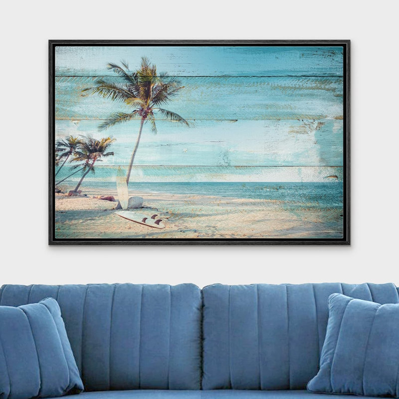 Coastal beach scene wall art in a black frame hanging above a blue sofa.