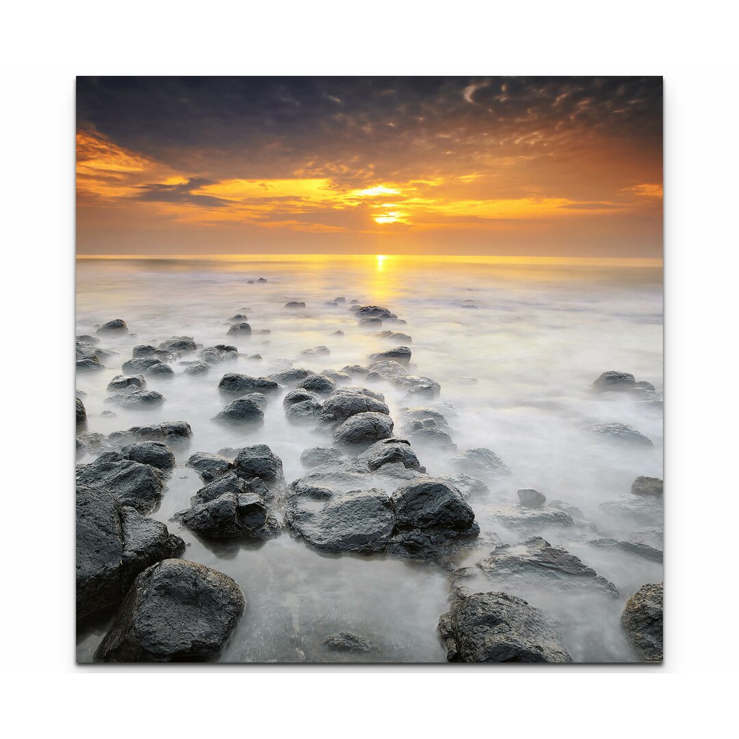 Leinwandbild Sonnenaufgang über einem Strand mit schwarzen Steinen