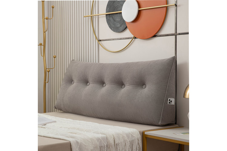 A rectangular backrest pillow with button-tufted detailing acting as the headboard on a headboard-free bed frame.