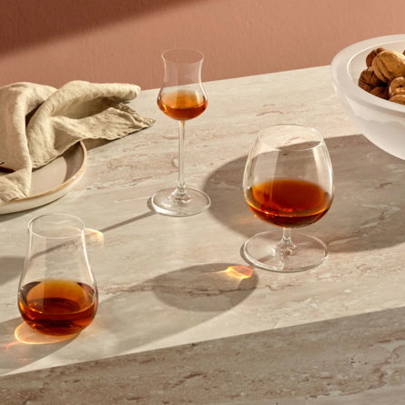 Three glasses of whiskey, a linen, plate, and bowl of walnuts on a marble surface.