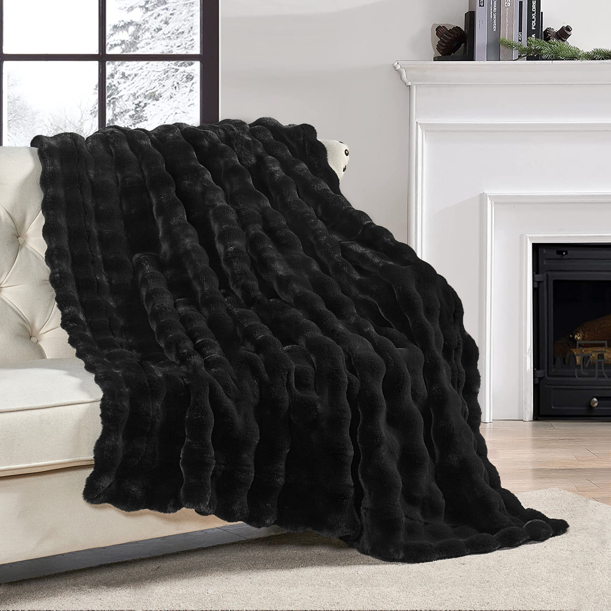 Plush black faux fur throw blanket draped over a cream tufted sofa in front of a fireplace and snowy window scene