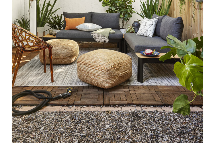 Outdoor space with a wood-tiled patio and patio furniture surrounded by plants and a gravel border.