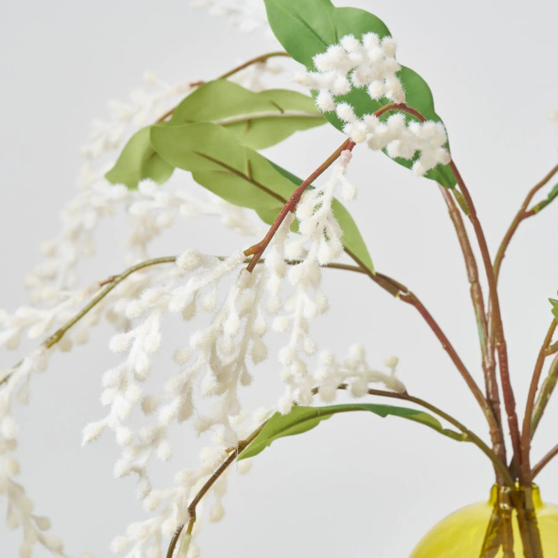 Branche de mimosa blanche floue dans un vase en verre de couleur verte
