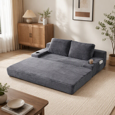 Canapé-lit 2 en 1 en velours côtelé gris de 180 cm de large, avec deux coussins décoratifs, porte-gobelets intégrés aux accoudoirs et sacs de rangement latéraux ; idéal pour les salons, les chambres et les coins détente.