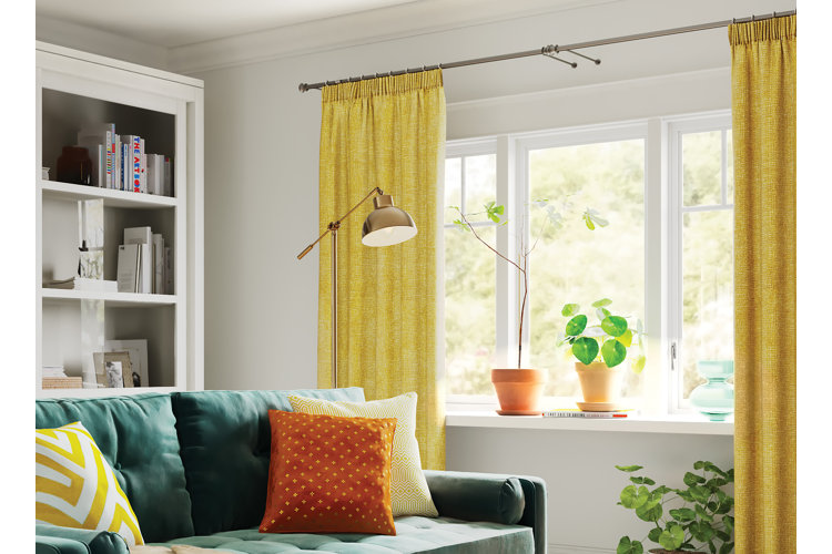 Living room with an emerald green sofa beside a large window with yellow curtains pulled back.