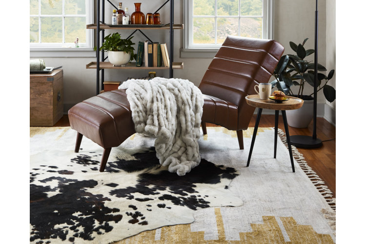 Cowgirl aesthetic room with a brown leather chaise lounge on top of a cowhide rug layered on top of a southwestern rug.
