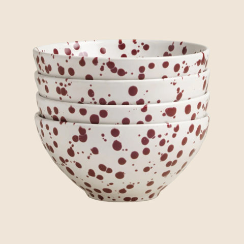 A stack of four white ceramic bowls featuring a decorative dark red splatter pattern.