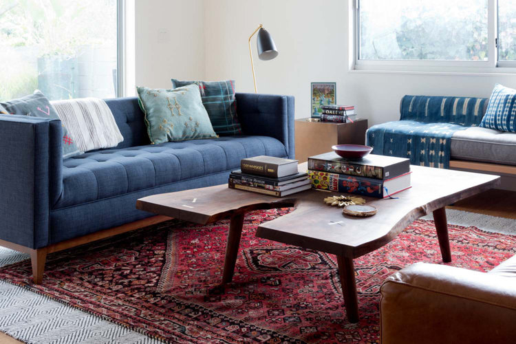 A trendy modern living room with a blue tuxedo sofa and a red oriental rug.