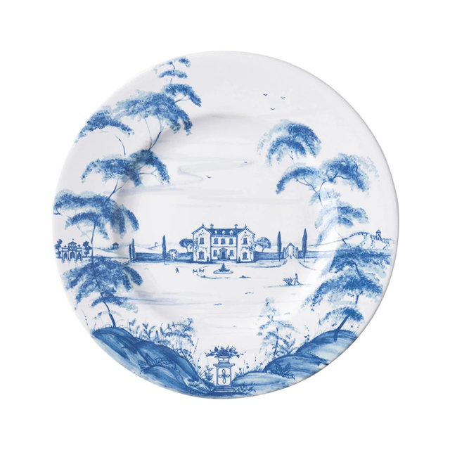 White ceramic dinner plate featuring a blue and white toile-style illustration of a countryside estate with trees and rolling hills.