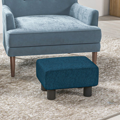 Le tabouret Blue Cube, en lin recouvert de solides pieds en plastique, ajoute du confort au repose-pieds en tissu bleu, créant une ambiance relaxante