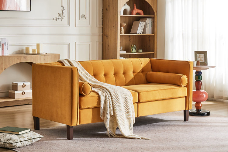 mustard yellow velvet sofa with button-tufted cushions and bolster pillows with cream knit throw blanket draped across back