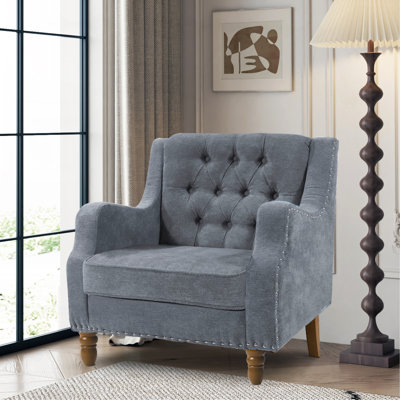 Chaise d'appoint grise avec dossier capitonné et pieds robustes, offrant confort et style pour votre maison