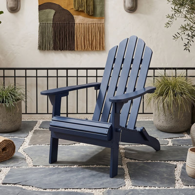 Chaise Adirondack pliable en bois d'acacia avec dossier à lattes, larges accoudoirs, idéale pour l'extérieur, sur une terrasse ou au bord d'une piscine.