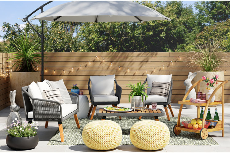 wood-and-wicker patio conversation set with a cantilever umbrella, patio bar cart, and a green outdoor rug