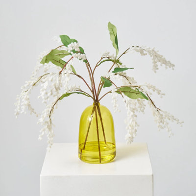 Branche de mimosa blanche floue dans un vase en verre de couleur verte
