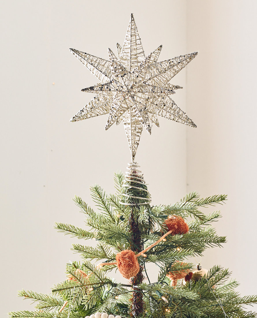Gros plan sur un sapin de Noël surmonté d'une étoile argentée.