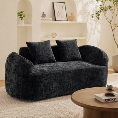 Canapé noir courbé pour deux personnes. Il a des accoudoirs des deux côtés, est livré avec deux coussins, convient aux petits appartements et peut être placé dans le salon ou la chambre à coucher.