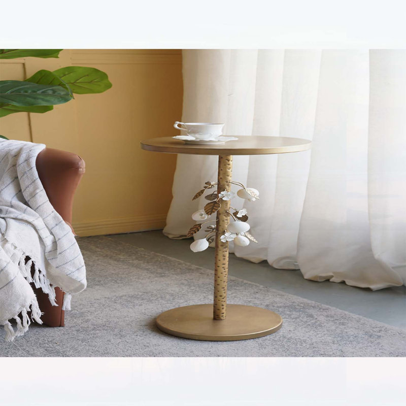 Table d'appoint ronde en fer avec accents floraux dorés et blancs, base en ciment et détails botaniques élégants pour les intérieurs modernes