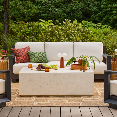 Outdoor seating area with off-white couch, concrete coffee table, and garden backdrop.