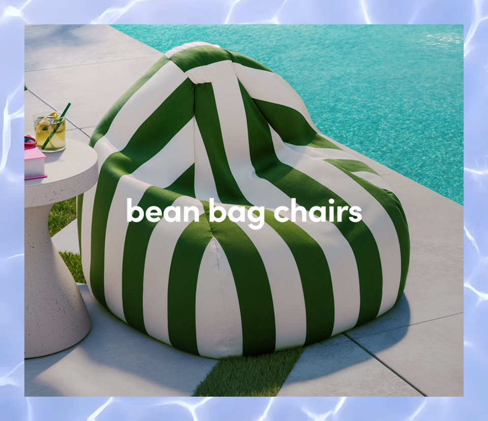 A green and white striped outdoor bean bag chair sits on a poolside patio next to a small side table and drink.