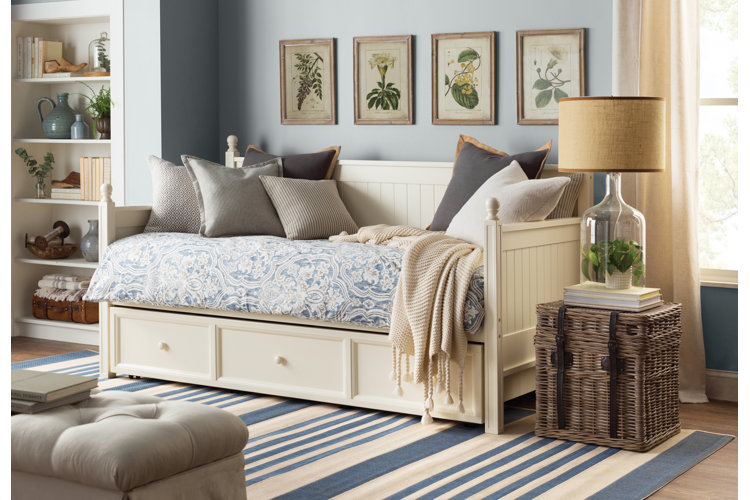 ivory wood daybed with a patterned blue comforter, gray throw pillows, and a cream knit blanket in a farmhouse-style living room