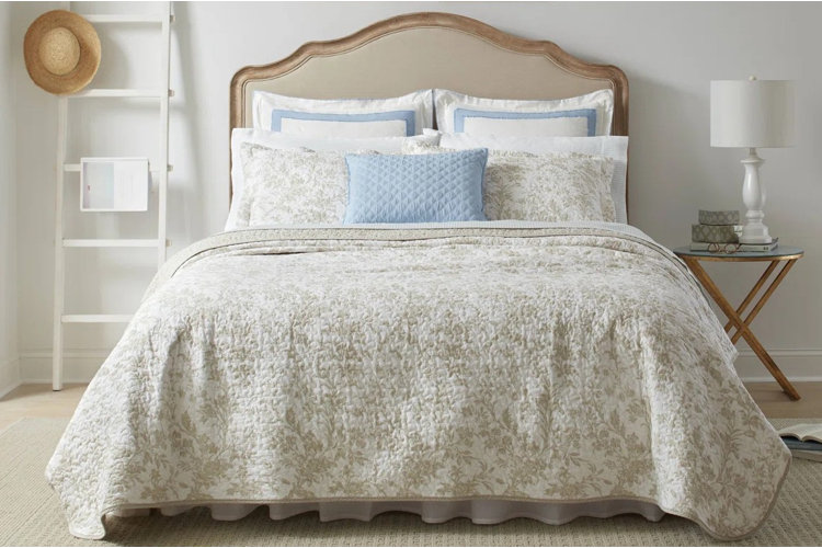 wood upholstered headboard with a beige floral bedspread and blue accent pillow in a traditional-style bedroom