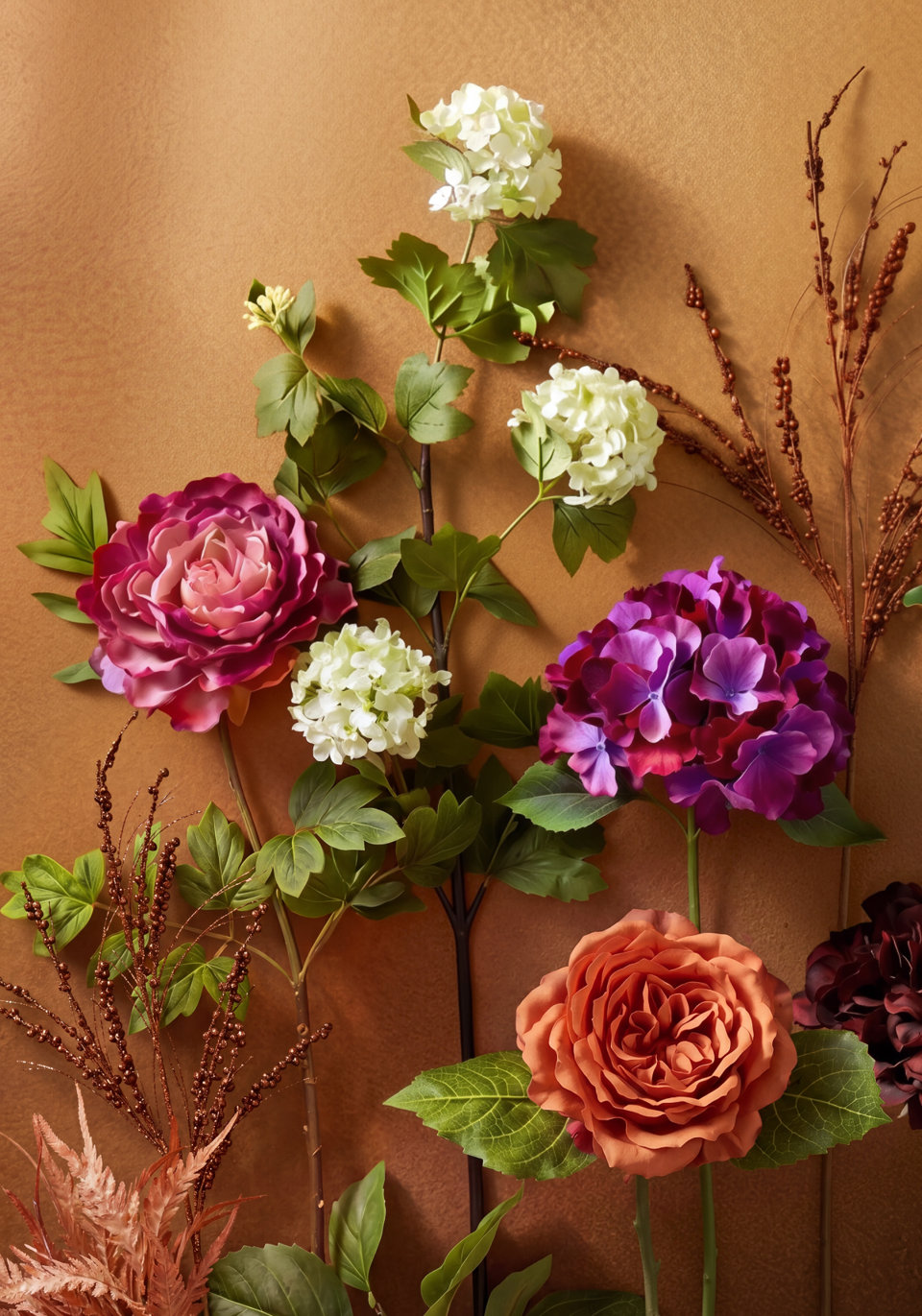 Artificial floral arrangement featuring a large fuchsia peony, a vibrant purple hydrangea, a terracotta-colored rose, and stems of light green hydrangeas and dried rustic branches set against a textured tan background.