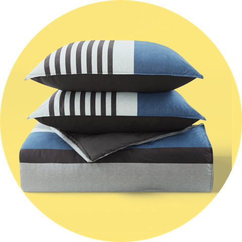 A folded blue, grey, and black colorblock comforter stacked with two matching pillows on a yellow background.