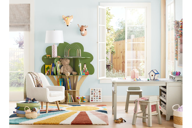 small kids playroom with light blue walls, a rainbow area rug, tree-shaped bookcase, and a white wood craft table