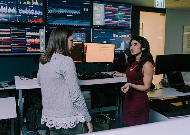 Two employees meeting in front of many screens displaying graphs