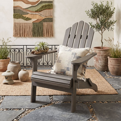 Chaise Adirondack pliable en bois d'acacia avec dossier à lattes, larges accoudoirs, idéale pour l'extérieur, sur une terrasse ou au bord d'une piscine.