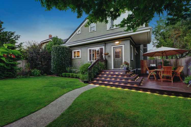 house with landscaped yard including a walkway, shrubbery, and a deck
