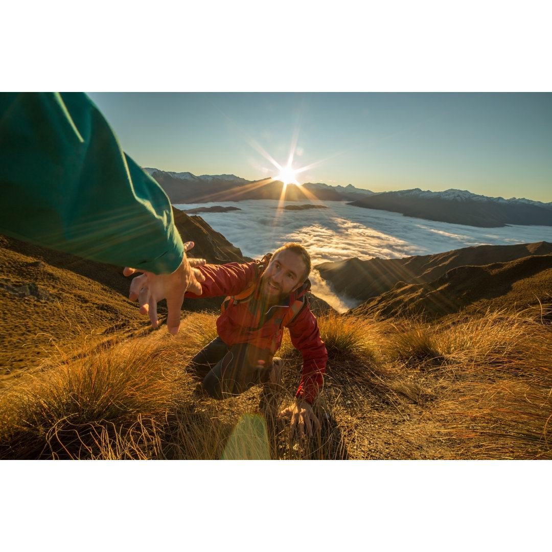 Wanderer, der seine Hand auf dem Berggipfel ausstreckt und um Hilfe bittet by Swissmediavision - No Frame Print on Canva...