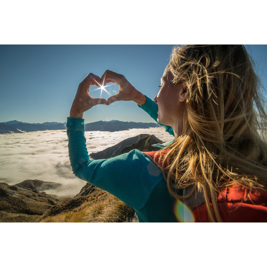 Junge Frau steht auf Berggipfel, rahmt Sonnenstrahl von Swissmediavision - No Frame Print on Canvas