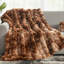 Brown faux fur throw blanket with a textured bubble wave design draped over a grey sofa.
