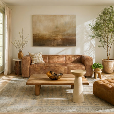 Quiet luxury style living room featuring a brown leather sofa, wooden coffee table, neutral color palette, abstract wall art, and lush indoor plants