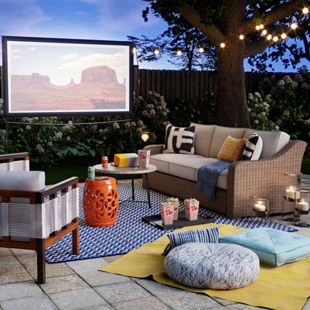 Outdoor movie night setup with couch, chair, screen, and string lights.