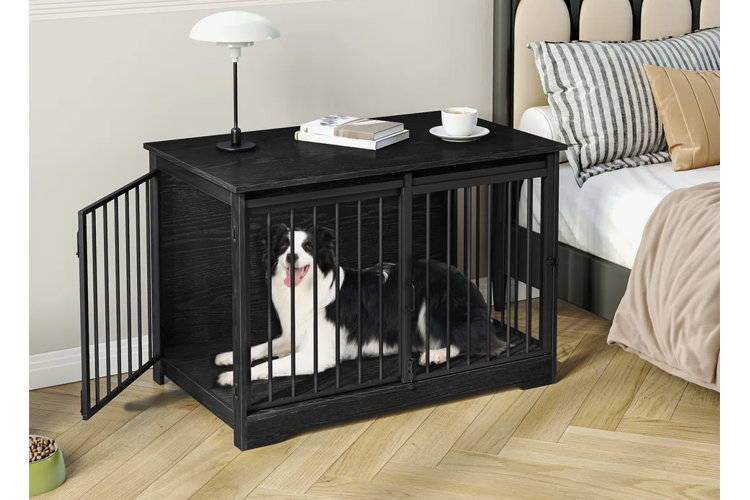 A multi-functional black wood furniture dog crate serving as a bedroom nightstand next to a bed, with a black and white border collie sitting comfortably inside behind its metal bars