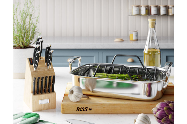 Kitchen island countertop with a knife set in a wood storage block beside a butcher block with a stainless steel roasting pan.