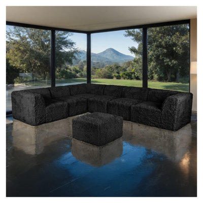 Ensemble de salon modulaire 7 pièces en L, couleur noire, garni de fausse fourrure et de mousse haute densité compressée, avec fauteuils sans accoudoirs et poufs.