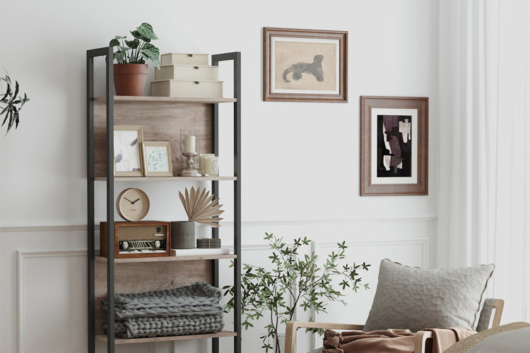 modern etagere with black frame and wood shelves styled with boxes, framed art, candles, and decorative accents beside chair and wall art