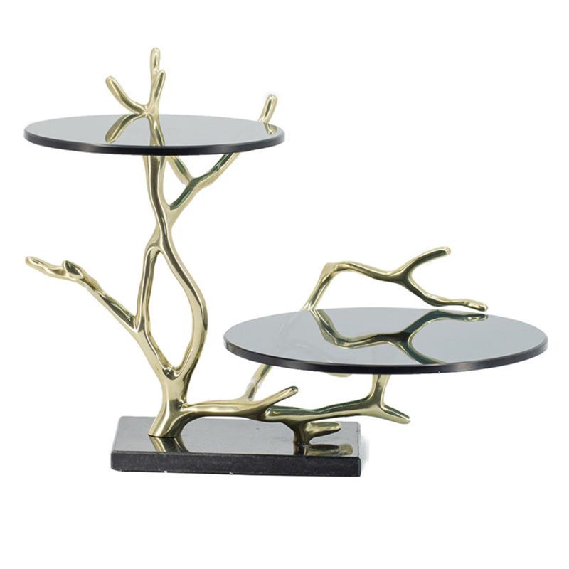 Présentoir à gâteaux à deux étages en forme de branche dorée, avec dessus en verre noir et base en granit.