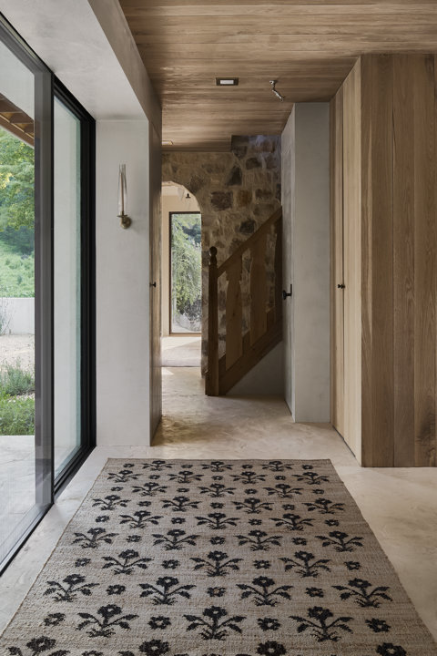 Un tapis de sol à motif floral placé dans une entrée moderne avec un plafond lambrissé de bois, des accents en pierre et un escalier.